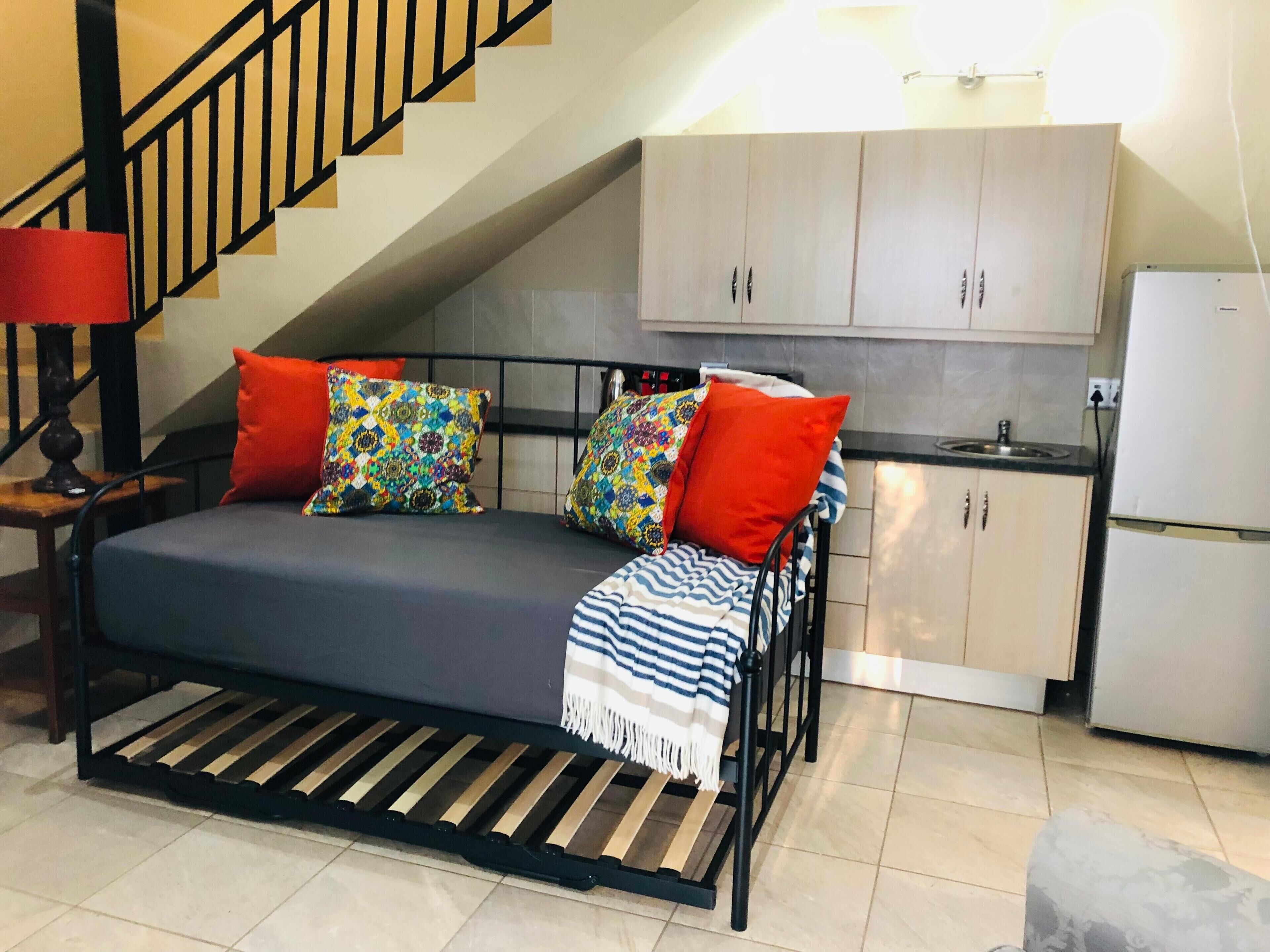 A compact room with a bed, a small kitchenette, and a staircase.