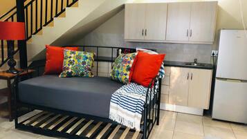 A compact room with a bed, a small kitchenette, and a staircase.