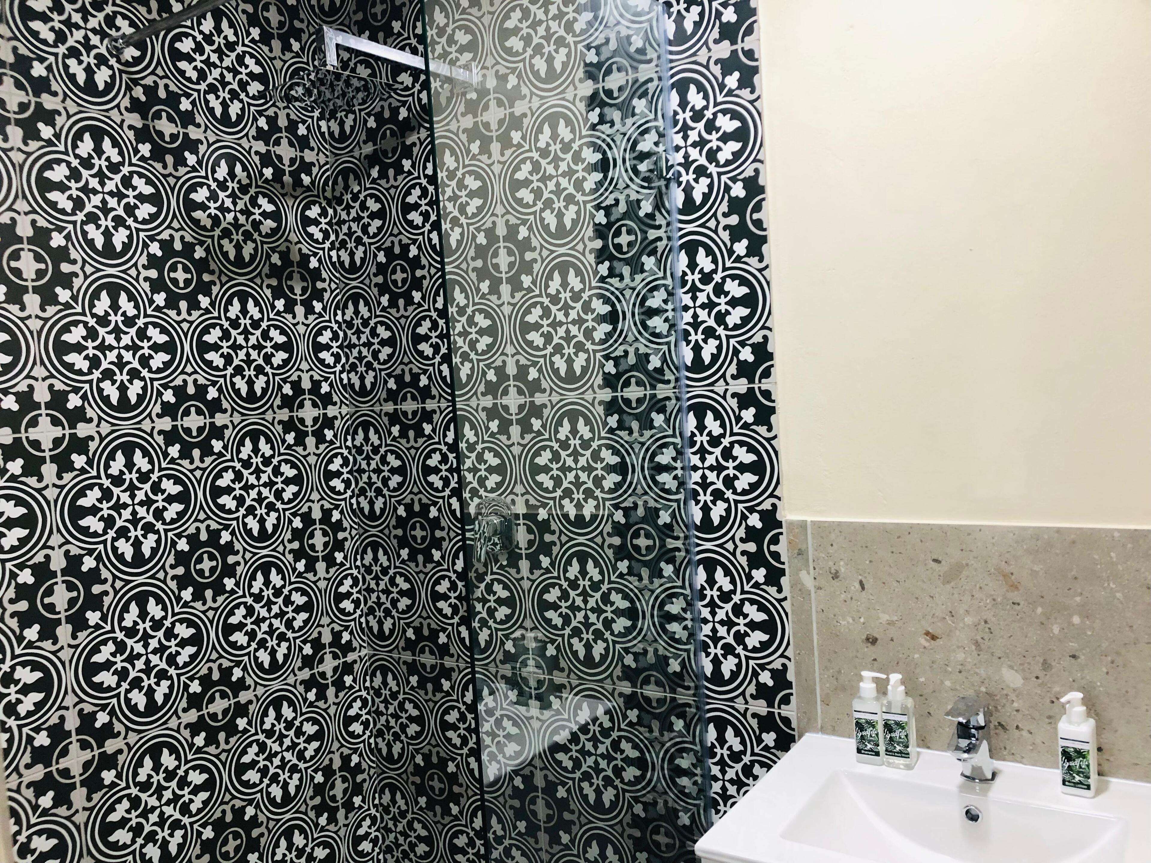 Un bagno con tenda da doccia a motivi bianco e nero, un lavandino bianco e tre flaconi di sapone per le mani.