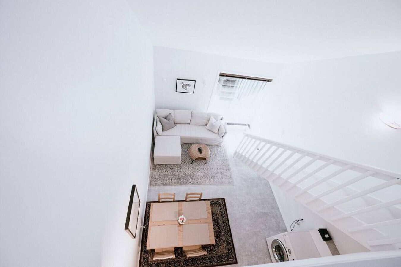 A modern, minimalist living room with a sofa, a small rug, and a staircase leading to another level.
