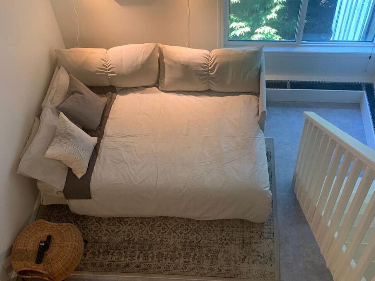 Ein Schlafzimmer mit Bett, Kissen, einem kleinen Teppich und einem Fenster mit Blick auf Bäume.