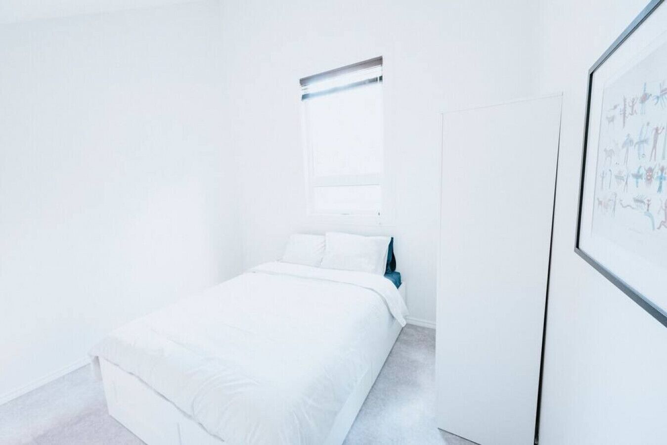 Quarto minimalista com uma cama, uma janela e uma obra de arte emoldurada na parede.