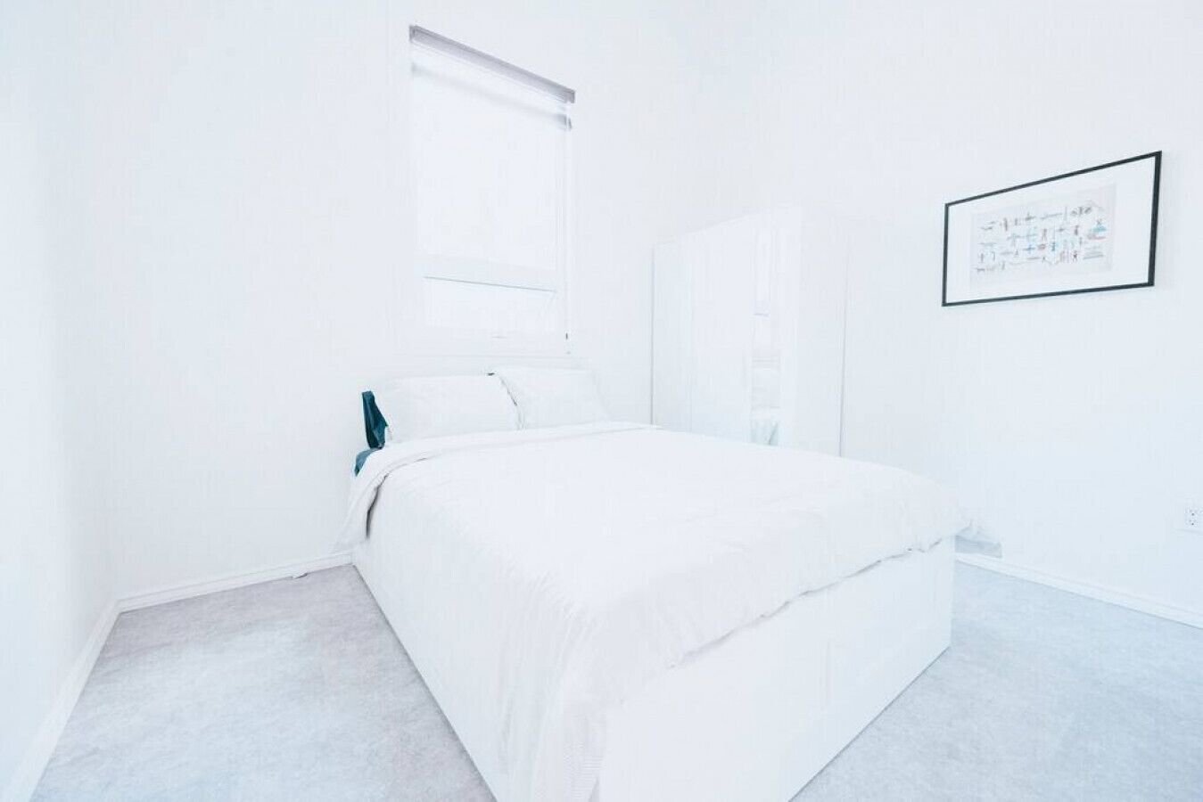 A minimalist bedroom with a bed, a window, and a framed picture on the wall.