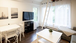 A modern living room with a white table, chairs, a flat-screen TV, and a sofa. - Mountainside 1BRM & Loft : Sleeps 4 ,Free Parking, Near Lakes, Restaurants & Shops! (Whistler)