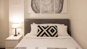 A neatly arranged hotel room with a bed, a bedside lamp, and a wall-mounted artwork. - Mountainside 1BRM & Loft : Sleeps 4 ,Free Parking, Near Lakes, Restaurants & Shops! (Whistler)
