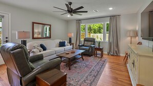 A spacious living room with a ceiling fan, a sofa, a coffee table, a leather chair, and a television on a cabinet. - Visiting professor?  New to area?  Perfect for you! (College Station)