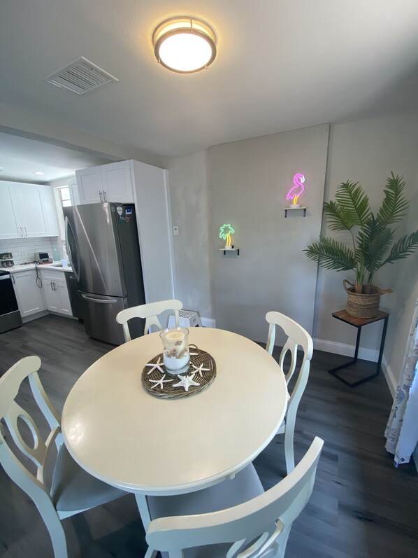 Una cocina moderna con armarios blancos, un refrigerador de acero inoxidable y un comedor con una mesa redonda y sillas blancas.