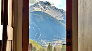 A door with a view of a mountain landscape, including snow-capped peaks and a forested valley.