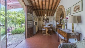 A rustic dining area with a wooden table and chairs, a chandelier, and a view of greenery outside. - Casa Anita (Castellina in Chianti)