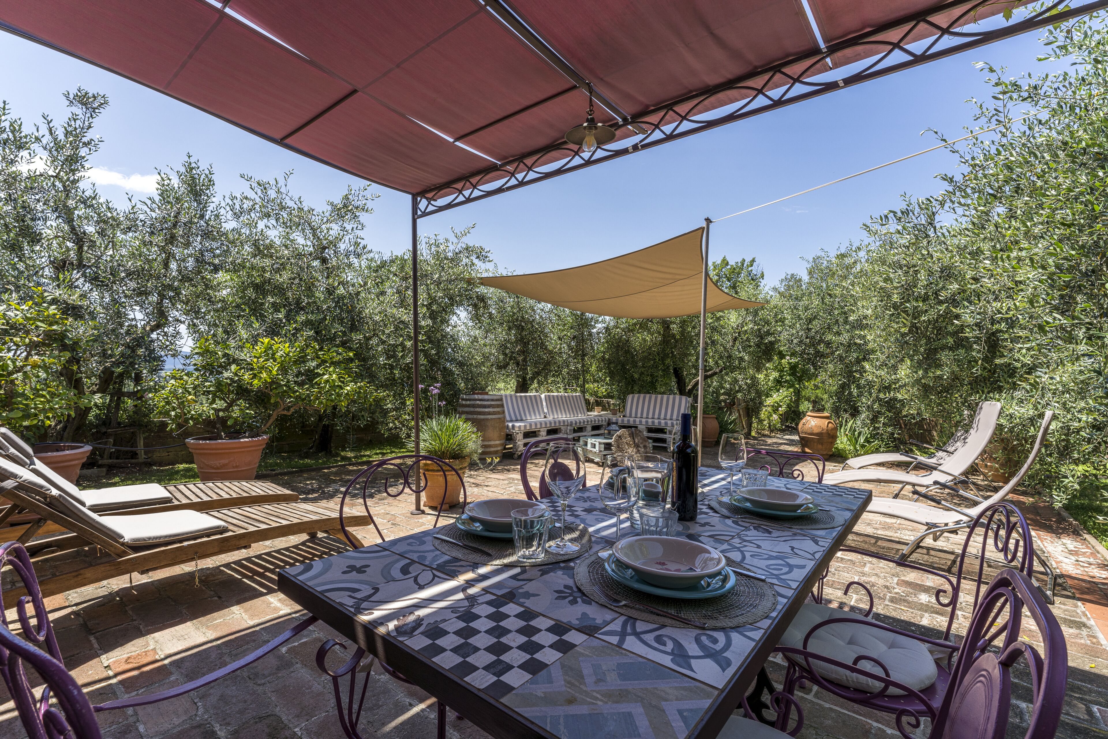 An outdoor dining area with a table set for four, surrounded by lounge chairs and a pergola providing shade.