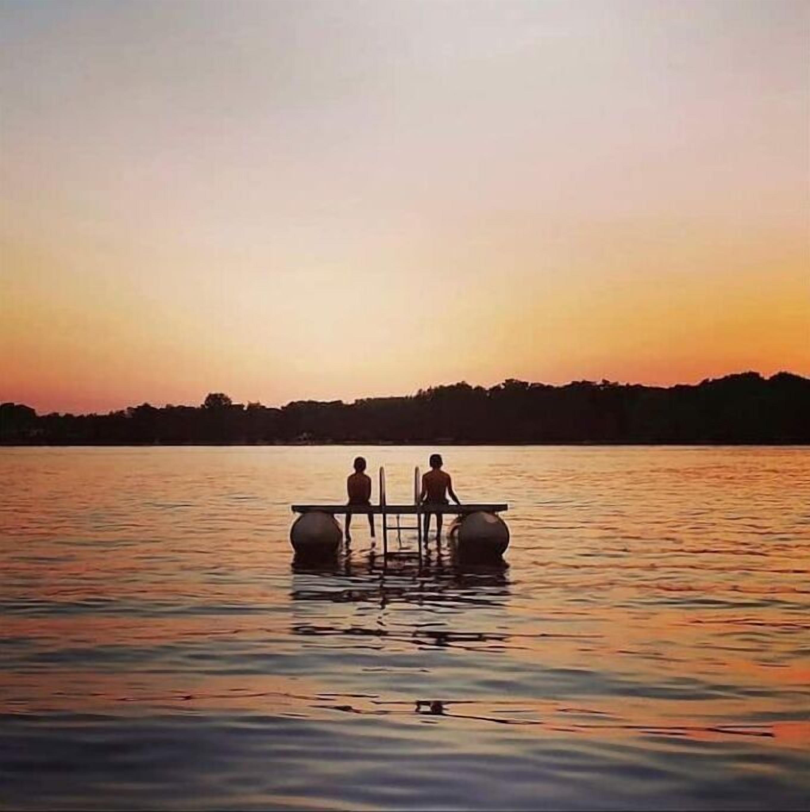 Un coucher de soleil sur un lac paisible, avec deux personnes sur un quai.