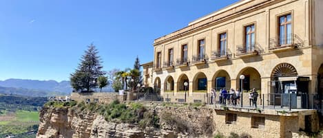 A hotel with a stone facade, arched windows, and balconies overlooking a cliff and valley.