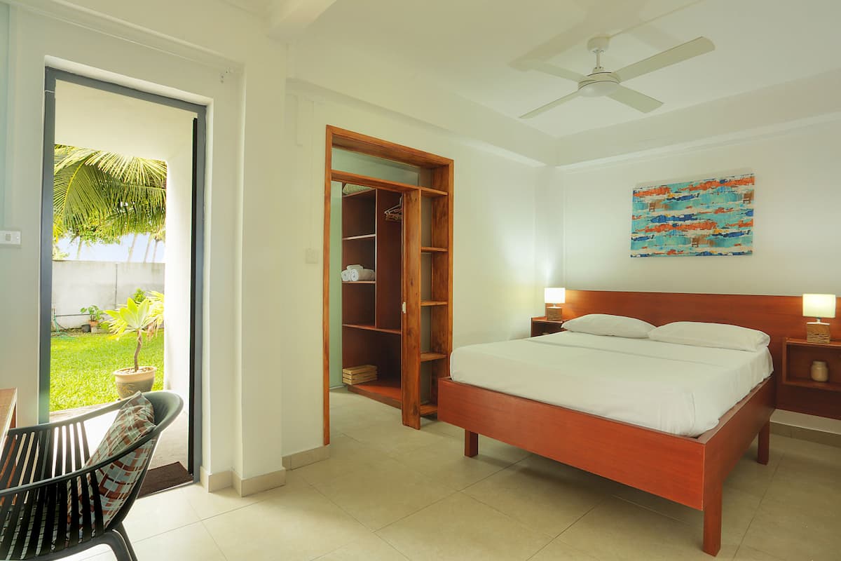 A bedroom with a bed, a wooden wardrobe, a ceiling fan, and a view of a garden.