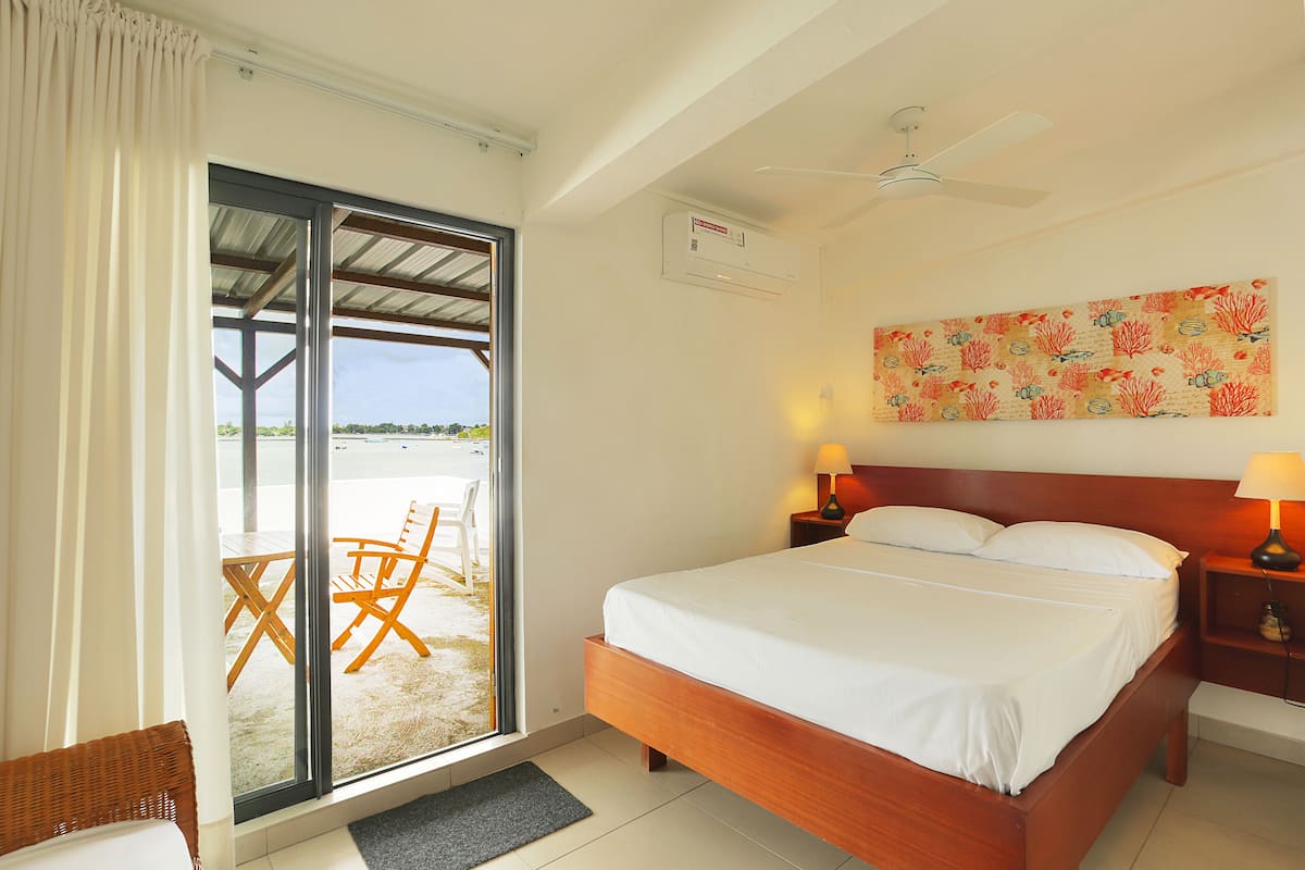 A hotel room with a large bed, a sliding glass door to a balcony, a ceiling fan, and a painting on the wall.