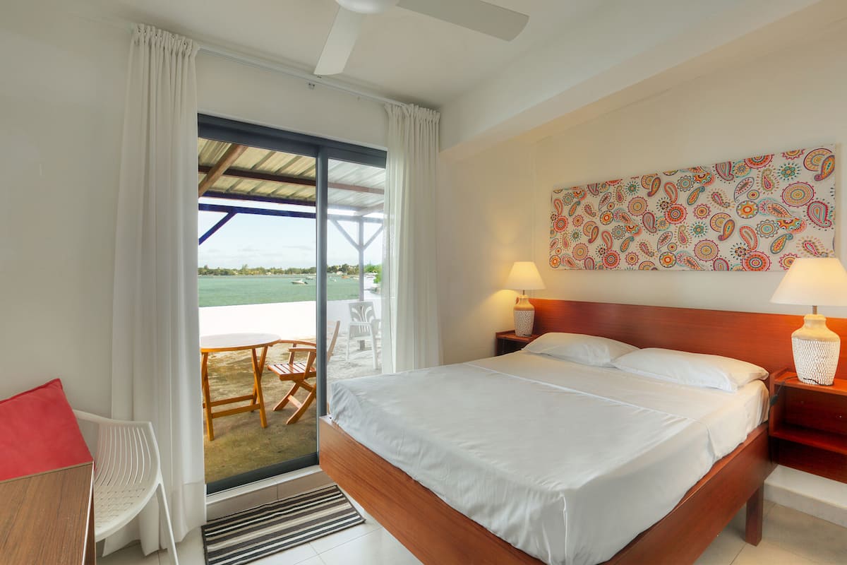 A hotel room with a bed, a chair, a table, and a view of the beach.
