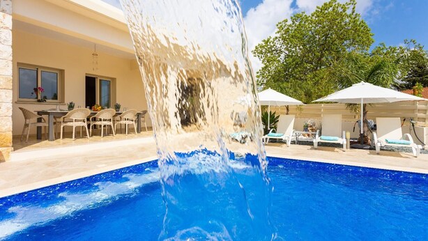 Une piscine agrémentée d’un élément décoratif aquatique, avec des espaces de détente en plein air et des parasols.