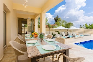 An outdoor dining area with a pool, wicker chairs, and a table set for two.