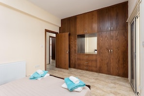 A bedroom with a large wooden wardrobe, a bed with rolled towels, and a radiator. - Villa Elite - Four Bedroom Villa, Sleeps 8 (Drouseia)