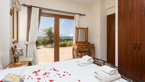 A bedroom with a bed, a wooden dresser, a mirror, and a view of the sea through a glass door. - Villa Erato - Three Bedroom Villa, Sleeps 6 (Nea Dimmata)
