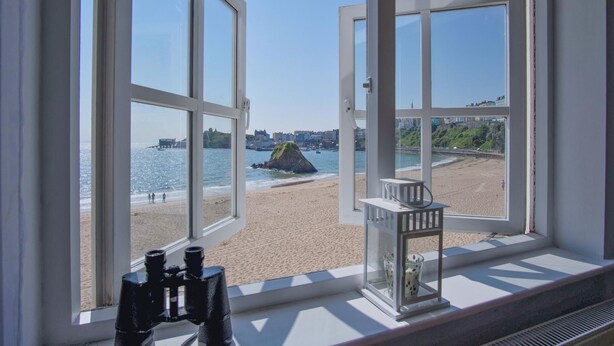 A room with large windows overlooking a beach, binoculars, and a lantern on the windowsill. - The Sand Castle - 2 Bedroom Apartment - Tenby (Tenby)
