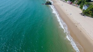An aerial view of a coastal town with a sandy beach, clear blue waters, and colorful buildings along the shore. - The Sand Castle - 2 Bedroom Apartment - Tenby (Tenby)