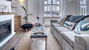 A modern living room with a fireplace, a large window with a view, a sofa, and a coffee table. - The Sand Castle - 2 Bedroom Apartment - Tenby (Tenby)
