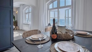 A dining table set with plates, glasses, and a bottle of wine, overlooking the sea. - The Sand Castle - 2 Bedroom Apartment - Tenby (Tenby)