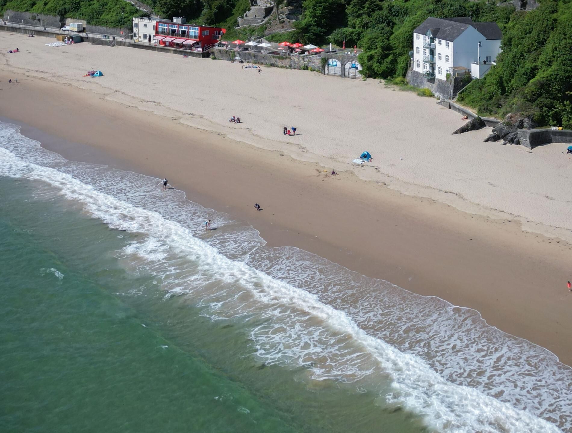 Ein Strand mit freiem Blick auf die Küstenlinie, einigen Personen und Gebäuden im Hintergrund.