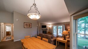 A dining area with a wooden table and chairs, a sofa, and a television in the background. - Lakefront 2BR Condo on Namakagon – Views, Trails, Pontoon Rentals & Fishing! (Cable)