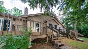 A modern house with a wooden staircase leading to a deck, surrounded by trees. - Lakefront 2BR Condo on Namakagon – Views, Trails, Pontoon Rentals & Fishing! (Cable)