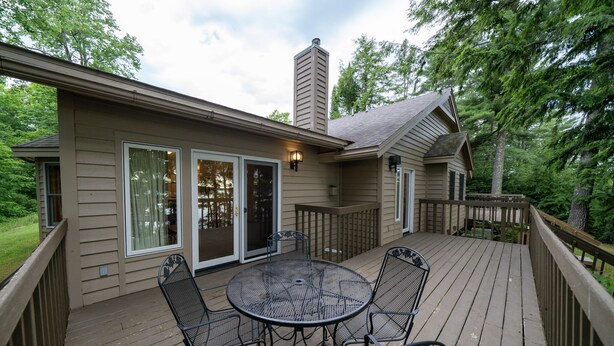 A deck with a round table and chairs, a sliding glass door, and a chimney. - Lakefront 2BR Condo on Namakagon – Views, Trails, Pontoon Rentals & Fishing! (Cable)