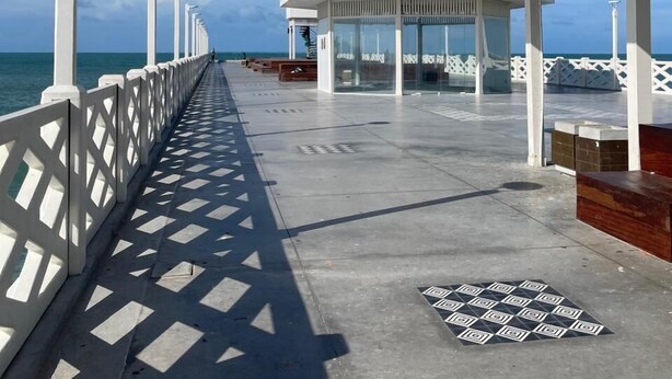 Une jetée avec une promenade dallée menant à une zone abritée équipée de sièges.