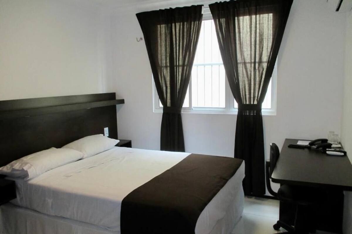 A hotel room with a bed, a desk, and curtains.