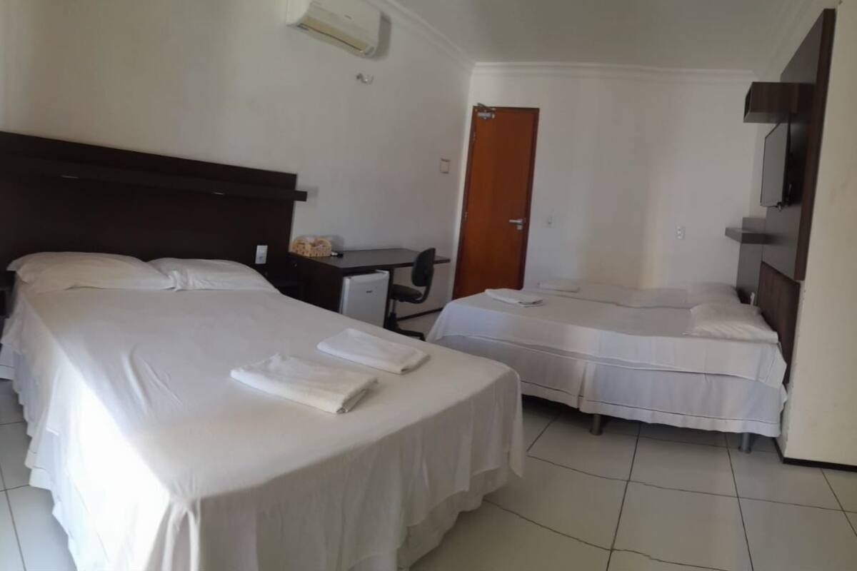 A hotel room with two single beds, a desk, a chair, a wardrobe, and a door.