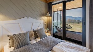 A bedroom with a large window, a bed with patterned pillows, and a view of the outdoors. - Apartament RELAKS (Zakopane)