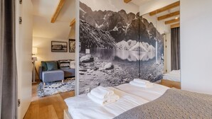 A bedroom with a large bed, a sofa, a mirror, and a wall with a mountain landscape mural. - Apartament RELAKS (Zakopane)