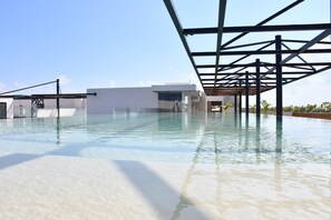 A modern pool area with clear water, a metal roof structure, and a white building in the background. - Palais Tulum by the Spot Rentals (Tulum)