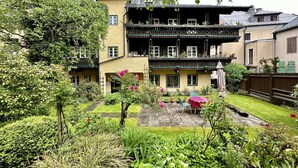 Edifici de dues plantes amb un balcó al pis superior, envoltat de vegetació abundant i un jardí ben cuidat.