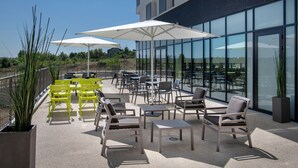 Une terrasse extérieure avec des chaises jaunes et grises, des parasols blancs et une vue sur la ville à travers de grandes fenêtres.