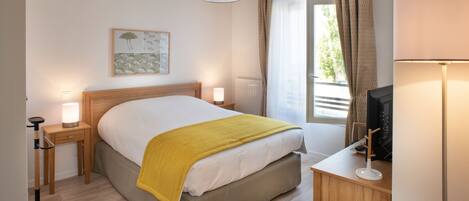 A hotel room with a bed, bedside lamps, a desk with a television, and a window with curtains.