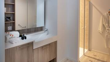 Een moderne badkamer met een witte wastafel, houten kastjes, een grote spiegel en een douchecabine met glazen wanden.
