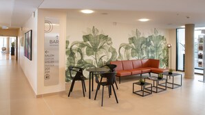 Un intérieur moderne avec un canapé rouge, des chaises noires et de petites tables. On peut voir une fresque murale représentant des feuilles vertes.