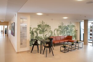 Un interior moderno con un sofá rojo, sillas negras y pequeñas mesas. Se aprecia un mural en la pared con hojas verdes.