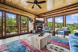 A spacious wooden interior with a fireplace, large windows, and a ceiling fan.