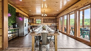 A spacious kitchen with wooden cabinets, a stainless steel refrigerator, and a dining area with a long table set for six. - Luxury Views, Sparkling Pool, Giant Theater Oh My! (Sevierville)