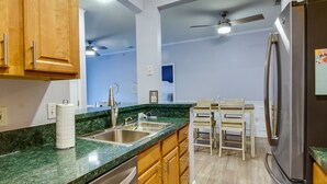 A modern kitchen with a green marble countertop, stainless steel appliances, wooden cabinets, and a dining area with a table and chairs. - Condo w/ Pool Access ~ 2 Mi to Rehoboth Beach! (Rehoboth Beach)