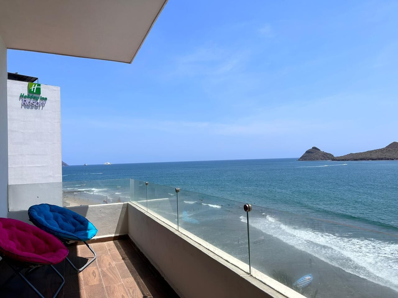Un balcón con vista despejada al océano, a una playa y el cartel de un complejo turístico.