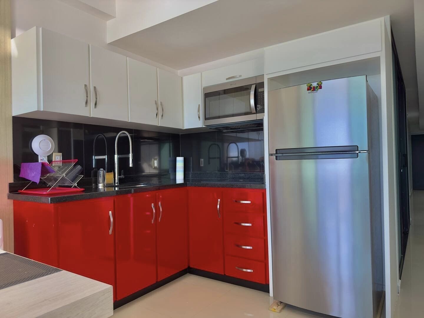 A kitchen with red cabinets, a stainless steel refrigerator, and a black countertop.