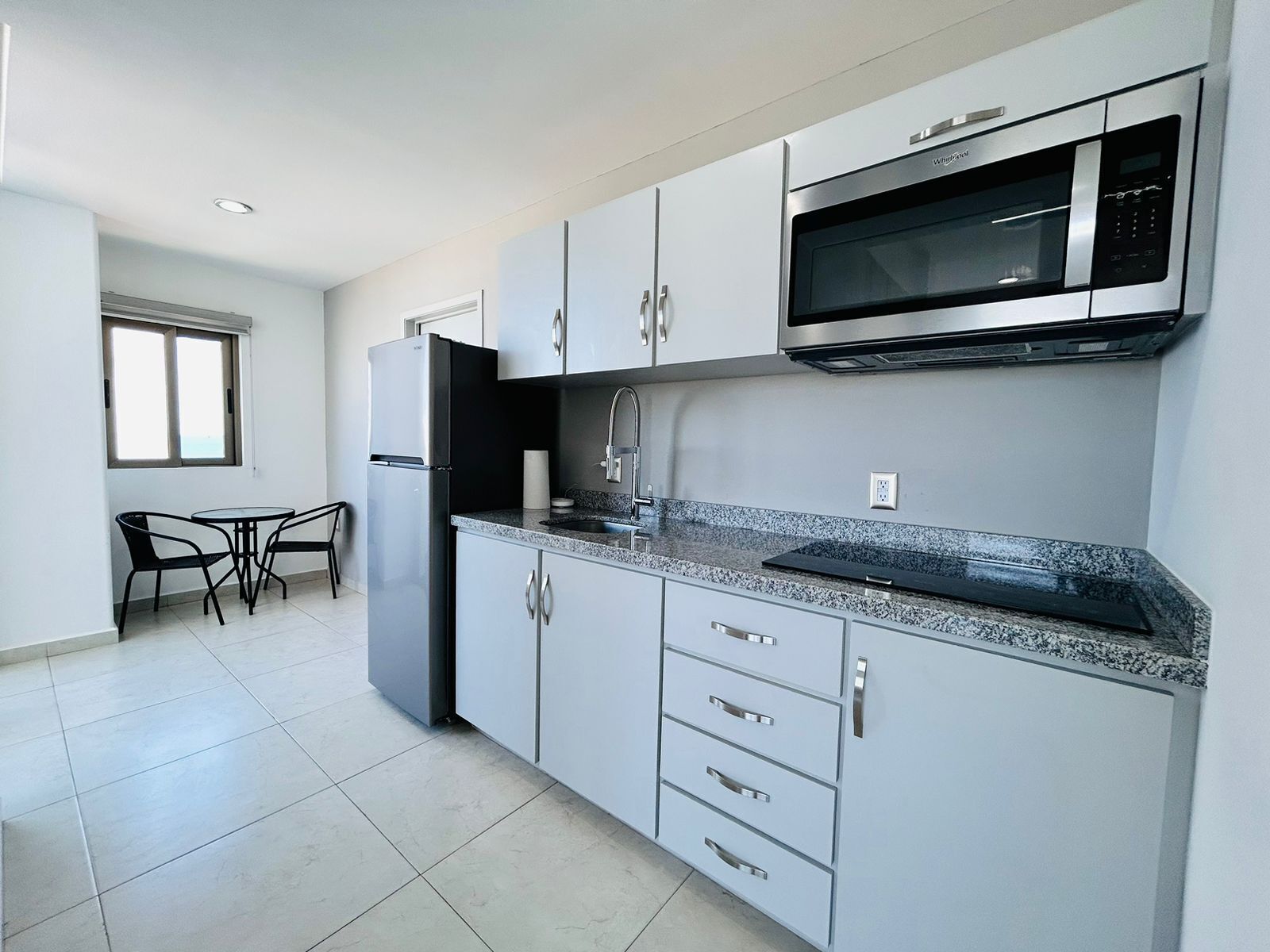 A modern kitchen with grey cabinets, a stainless steel refrigerator, a microwave, and a granite countertop.