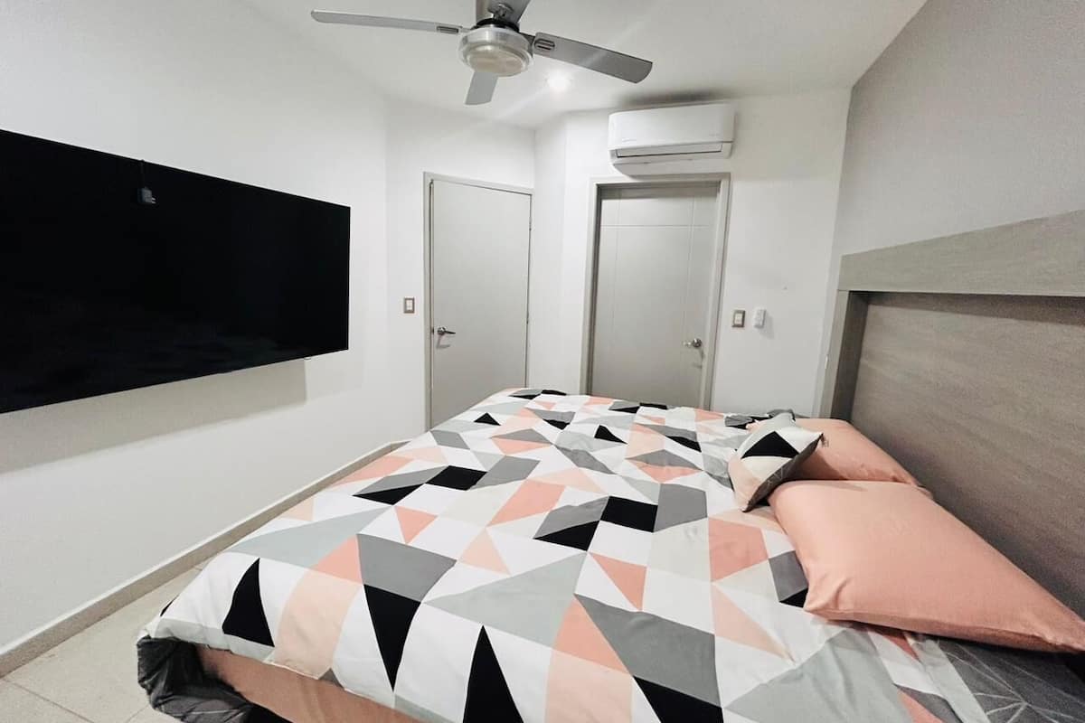 A bedroom with a bed, a ceiling fan, a TV mounted on the wall, and two doors.